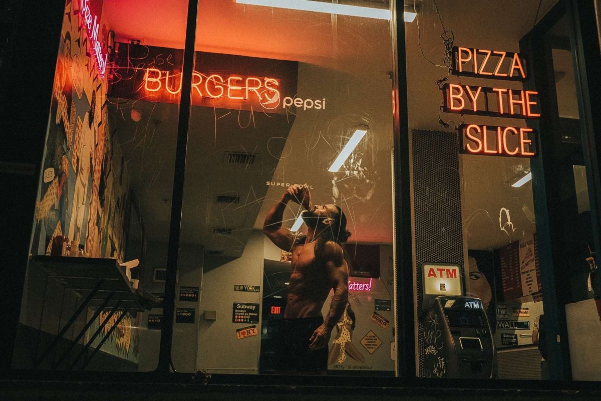 Homem a beber diante da montra iluminada de uma pizzaria